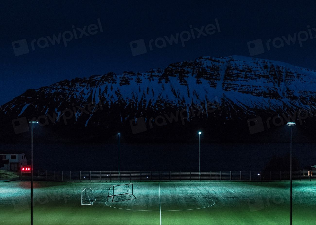 A floodlit pitch at dusk below a mountain ridge