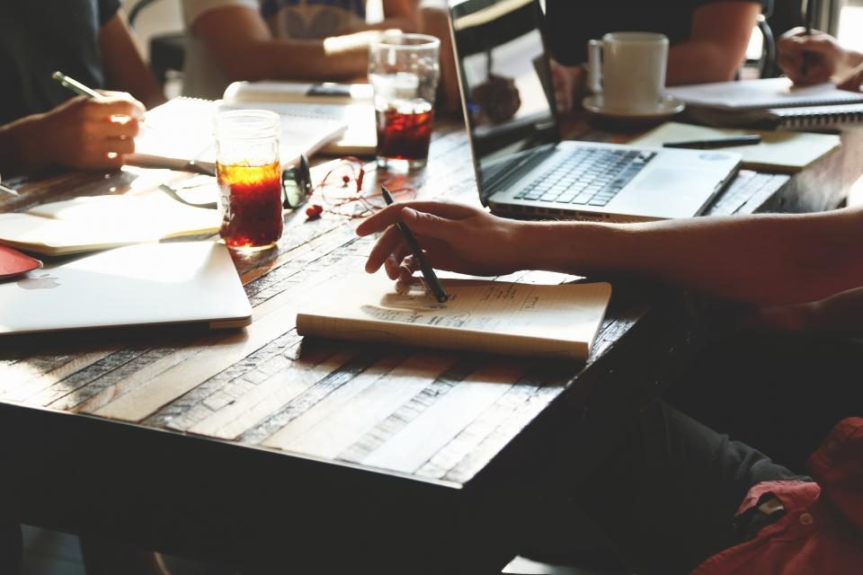 Notebooks, drinks and a laptop on a shared work table